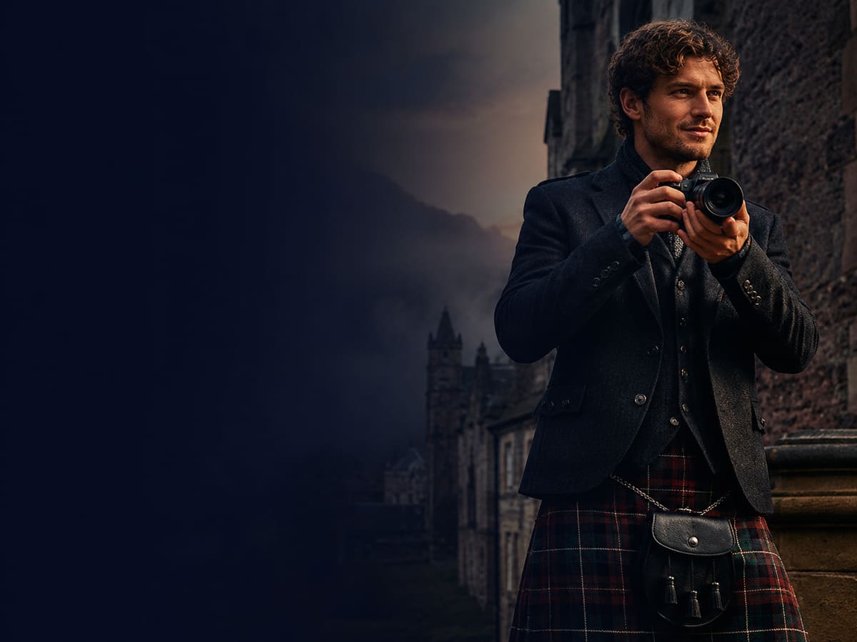 A man in a tartan kilt holding a camera on a wall in Edinburgh